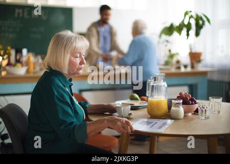 Ältere Frau, die im Pflegeheim frühstücken und Zeitung lesen kann. Stockfoto