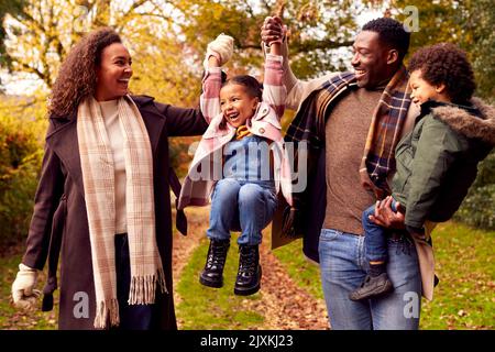 Smiling Family Having Fun Swinging-Tochter Auf Einem Spaziergang Durch Die Landschaft Gegen Herbstbäume Stockfoto