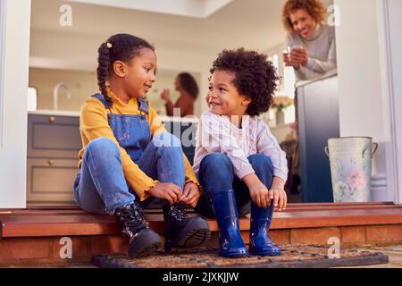 Kinder, Die Zu Hause Auf Der Stufe Sitzen, Ziehen Stiefel An, Bevor Sie Mit Großeltern Auf Einen Familienspaziergang Gehen Stockfoto