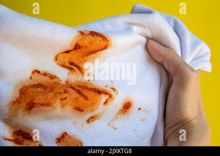 Lebensmittelflecken auf dem Hemd. Hand hält schmutziges T-Shirt. Stockfoto