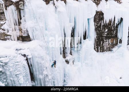 Eine Person, die sich am Johnston Canyon, Banff, auf einem großen gefrorenen Wasserfall mit riesigen Eiszapfen abseilt Stockfoto