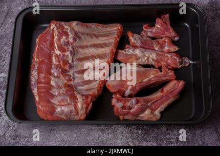 Rohe Schweinefleischrippen auf einem schwarzen Tablett, das zum Braten im Ofen bereit ist Stockfoto