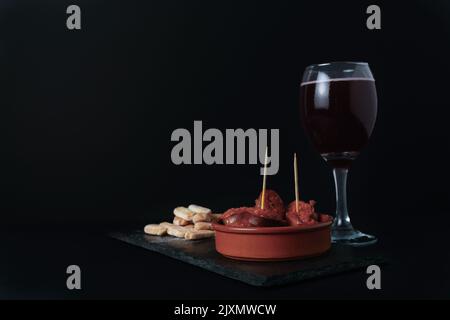 Nahaufnahme einer Tapa mit Chorizo in Sauce, typisch spanischer Wurst mit Brot und Sommerrot auf schwarzem Hintergrund Stockfoto