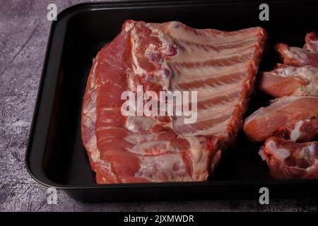 Rohe Schweinefleischrippen auf einem schwarzen Tablett, das zum Braten im Ofen bereit ist Stockfoto