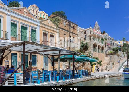 Symi, Griechenland - 26. August 2022: Panoramablick, Skyline der kleinen Oase der Insel Symi. Dorf mit Street Cafe und bunten Häusern auf Felsen. Stockfoto