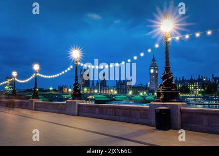 Lampenpfosten, die nachts auf dem Queen's Walk beleuchtet werden, Blick auf den Westminster Palast und den Big Ben in London, Großbritannien Stockfoto