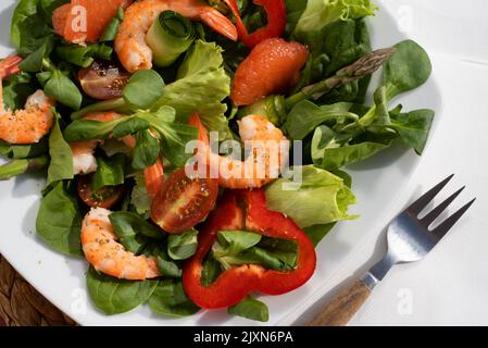 Frische Salatplatte mit Garnelen, Gurken, frischem Spargel, Tomaten und gemischtem Gemüse auf einem Holztisch. Gesunde Ernährung Stockfoto