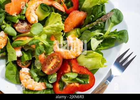 Frische Salatplatte mit Garnelen, Gurken, frischem Spargel, Tomaten und gemischtem Gemüse auf einem Holztisch. Draufsicht. Gesunde Ernährung Stockfoto