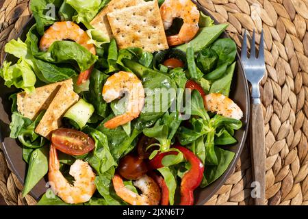 Frische Salatplatte mit Garnelen, Gurken, frischem Spargel, Tomaten und gemischtem Gemüse auf einem Holztisch. Draufsicht. Gesunde Ernährung Stockfoto