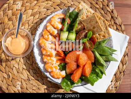 Frische Salatplatte mit Garnelen, Gurken, frischem Spargel, Tomaten und gemischtem Gemüse auf einem Holztisch. Draufsicht. Gesunde Ernährung Stockfoto