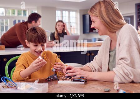 Mutter Hilft Sohn Mit Elektronik-Projekt Sitzen Am Küchentisch Zu Hause Mit Laptop Stockfoto