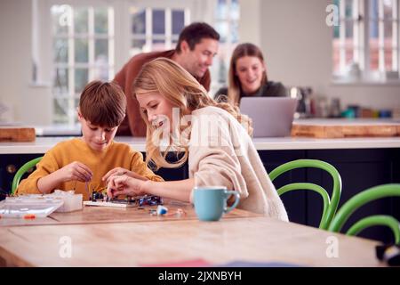 Mutter Hilft Sohn Mit Elektronik-Projekt Sitzen Am Küchentisch Zu Hause Mit Laptop Stockfoto