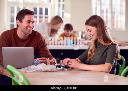 Vater Hilft Teenage-Tochter Mit Elektronik-Projekt Sitzen Am Küchentisch Zu Hause Mit Laptop Stockfoto