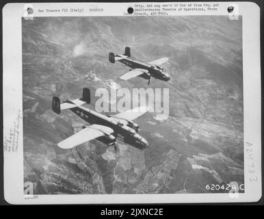 Bomben, die von der nordamerikanischen B-25 Mitchells der 12. Air Force abgeworfen wurden, explodieren auf Einer Eisenbahnbrücke in Italien. Zwei Mitchells Fliegen Hoch Über Dem Rauchziel. Stockfoto