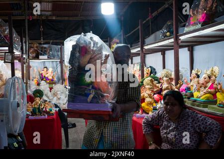 Ein Mann, der ein Ganpati-Idol in einer Werkstatt von Lord Ganesha-Idolen in Mumbai vor dem verheißungsvollen indischen Fest von Ganesh Chaturthia trägt Stockfoto