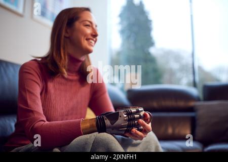 Nahaufnahme Einer Frau Mit Einem Prothetischen Arm Und Einer Hand, Die Sich Zu Hause Auf Dem Sofa Entspannt Und Eine Tasse Kaffee Trinkt Stockfoto