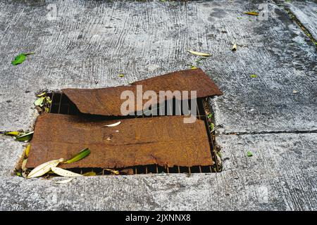 Die Ansicht der alten verrosteten Metallplatte wurde von oben verwendet, um das zerbrochene Stahlgitter der Abdeckung des Straßenabflusses zu bedecken. Verrostete Stahlblechabdeckung auf beschädigtem Ablaufgitter. Sa Stockfoto