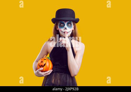 Frau im halloween Kostüm mit gruseligen Make-up in Hut zeigt Stille Geste auf gelbem Hintergrund. Stockfoto