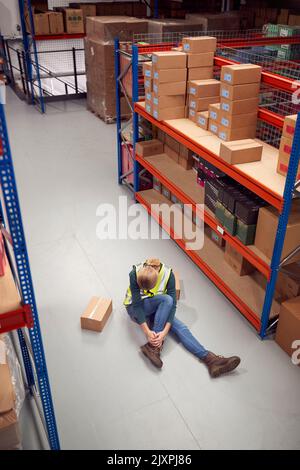 Weibliche Arbeiterin Mit Verletztem Bein Auf Dem Boden Nach Einem Arbeitsunfall Im Lager Stockfoto