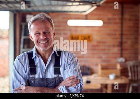 Portrait Von Lächelnd Reifen Mann Tragen Overalls In Garage Workshop Stockfoto