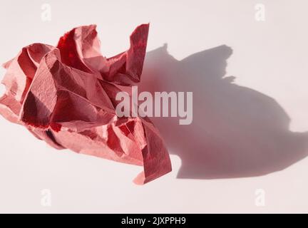 Eine zerknitterte Papierkugel aus rosa Papier und deren Schatten auf hellem Hintergrund, Draufsicht. Stockfoto