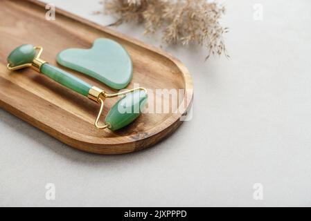 Massage-Walzen für Gesichts-Jade und Massagegerät Gua Sha aus natürlichem Jadestein auf hellem Betongrund, Draufsicht Stockfoto
