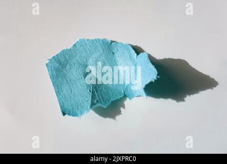 Ein Stück blaues Papier oder zerrissene Papierstücke mit hartem Schatten auf weißem Hintergrund, Draufsicht. Stockfoto