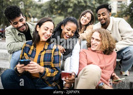 Junge Gruppe von multirassischen Studentenfreunden, die in der Stadt ein Mobiltelefon benutzen Stockfoto