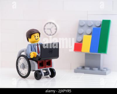 Tambow, Russische Föderation - 6. September 2022 Ein Lego-Geschäftsmann minifigur im Rollstuhl, der in seinem Büro einen Laptop benutzt. Stockfoto