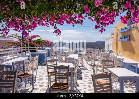 Leeres griechisches Terrassenrestaurant mit wunderschönen rosa Bougainvilleas und einer tollen Aussicht. Urlaubsziel Kykladen Inseln in Aegean Sea, ​​Greece. Stockfoto