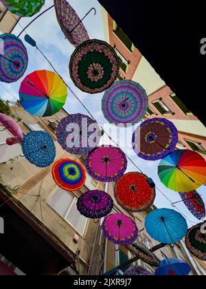Bunte Hängebschirme in verschiedenen Designs und Formen, die zwischen Wohnwohnungen in einem Stadtteil in Istanbul, Türkei, direkt darüber hängen. Stockfoto