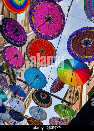 Bunte Hängebschirme in verschiedenen Designs und Formen, die zwischen Wohnwohnungen in einem Stadtteil in Istanbul, Türkei, direkt darüber hängen. Stockfoto