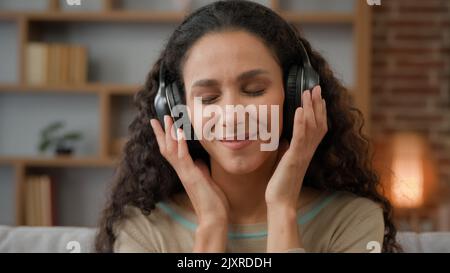 Vorderansicht Nahaufnahme lächelnde hispanische Frau mit lächelndem Lächeln, die Dame, die sich zu Hause mit geschlossenen Augen entspannt und Musik im Kopfhörer-Audio hört Stockfoto