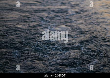 Nahaufnahme von Wasserwellen, die von einem Boot, das in der Dämmerung einen Bach überquert, gemacht wurden. Horizontaler Hintergrund oder Kopierraum für Entspannung, Urlaub, Ruhe und Meditation. Stockfoto