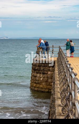 Touristen, die am Ende einer Anlegestelle in der swanage Bay in dorset, großbritannien, stehen Stockfoto