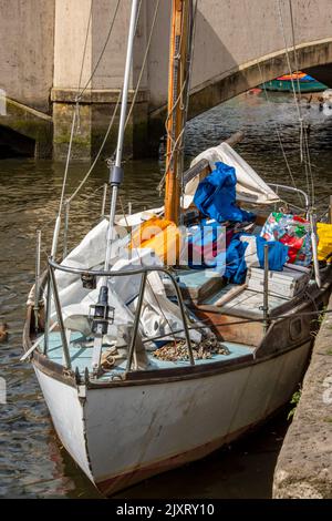 Verquälte alte hölzerne Segelyacht an einer Wand, die aufgeräumt und gearbeitet werden muss, alte traditionelle hölzerne Segelyacht, die in einem Hafen oder Hafen festgebunden ist. Stockfoto