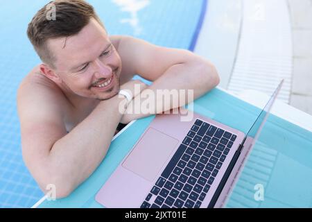 Junger, hübscher Mann im Pool mit Laptop Stockfoto