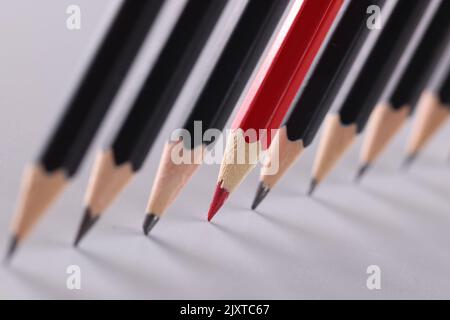 Roter Bleistift trennt eine Reihe von schwarzen Bleistiften Stockfoto