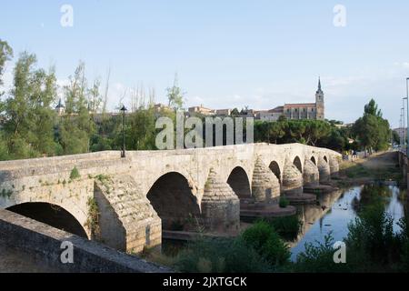 Alte Steinbrücke über den Fluss Arlanza bei Lerma, Burgos. Stiftskirche von San Pedro in der Ferne. Stockfoto