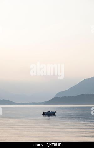 Einsamer Fischer in einem Boot an einem ruhigen, friedlichen Morgen auf dem Comer See, Italien. Stockfoto