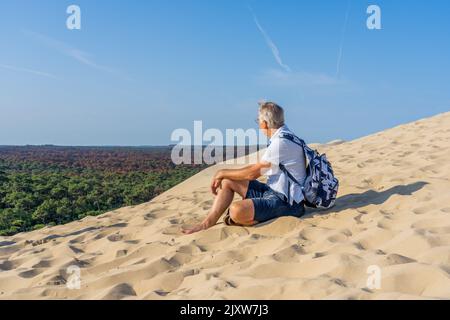 Mann sitzt auf einer riesigen Sanddüne, berühmtes Touristenziel Dune Pyla. Pilat Dune in Frankreich. Hochwertige Fotos Stockfoto