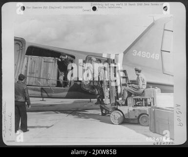 GIS, die Hunderte von Tonnen von Air Technical Service Command Air Freight-Sendungen abgewickelt haben, und die französischen Transportcrewmen arbeiten Seite an Seite, um eine riesige Thunderbolt Engine in Eine Douglas C-47 zu laden. C-47S an das französische Luftkorps überstellt und bemannt von Stockfoto