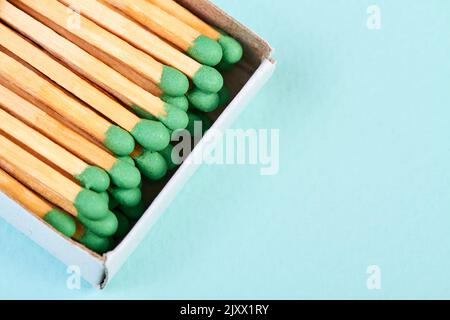 Viele Streichhölzer mit grünen Köpfen in einer Streichholzschachtel auf blauem Hintergrund mit Kopierraum Stockfoto