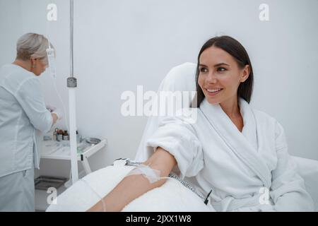 Schöne Frau im weißen Bademantel während der medizinischen Prozedur in der Schönheitsklinik Stockfoto