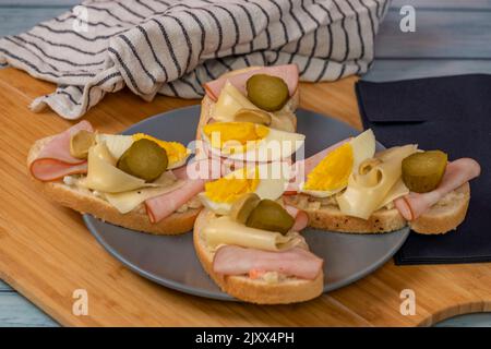 Typisches tschechisches offenes Sandwich mit Eiern, Kartoffelsalat, Schinken, Käse und Gurken auf einem blauen Holztisch Stockfoto