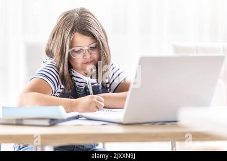 Mädchen in der Brille schreibt Notizen, die über Fernunterricht über das Internet studierten. Stockfoto