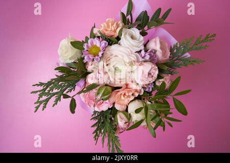 Blick von oben. Auf einem Strauß Rosen, Ranunculus, Nelke, Wacholder, bush Chrysantheme auf einem rosa Hintergrund. Mit einem zu kopierenden Leerzeichen. Ein Element für Ihr Design. Hochwertige Fotos Stockfoto