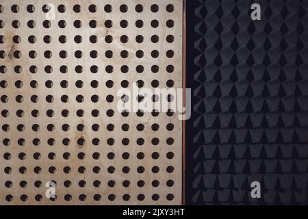 Holzoberfläche mit runden Löchern und schwarzer Schallschutzwand mit Akustikschaumstoff. Textur, Muster, Hintergrund. Stockfoto