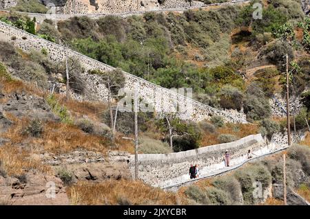 Fira, Santorini, Griechenland - 2022. Juni: Menschen, die den steilen Fußweg von der Stadt Fira zum Hafen am Fuße der Klippe hinuntergehen. Stockfoto