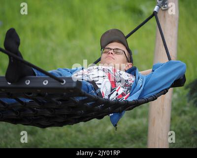 Ein junger Mann liegt auf einer Hängematte in einem Park oder Garten im Freien. Stockfoto